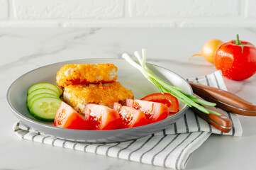 Fried breaded fish fillets withcucumper ant tomatoes served on a plate close up