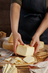 Wall Mural - Hands holding piece of  fresh homemade cheese on a wooden board