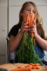 young girl in an apron in the kitchen with fresh carrots in her hands