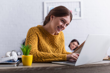 Wall Mural - happy teenage girl smiling while holding book near laptop