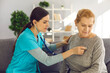 © Studio Romantic - Worried doctor with stethoscope checking sick female patient's heart at clinic office. General practitioner or EMS worker examining senior woman's lungs. Visit to hospital or paramedic's help at home