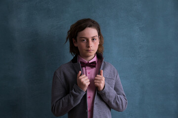 
Medium horizontal studio shot of cute preteen boy in pink shirt and bowtie holding the lapels of his grey coat