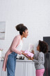 © LIGHTFIELD STUDIOS - side view of african american child presenting gift and greeting card to happy mom in kitchen