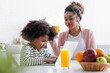 © LIGHTFIELD STUDIOS - smiling african american woman looking at concentrated daughter using laptop on blurred foreground