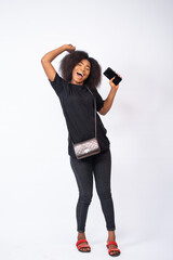 Wall Mural - excited and happy young black woman on a white background, rejoicing and holding a phone, advertising concept image