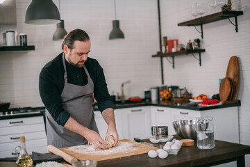 A male chef prepares dough at home in the kitchen