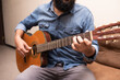 © Roy - Man dressed in casual clothes playing guitar, sitting on an armchair in a room
