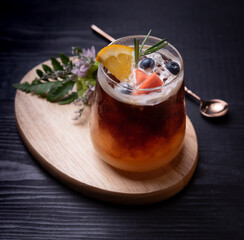 Sticker - glass of iced americano black coffee and layer of orange with rosemary,blueberries,orange and strawberry on wood