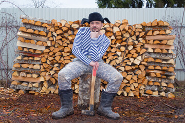 Sticker - a village man sits on a tree stump with an ax in his hands. in the background is a pile of chopped w