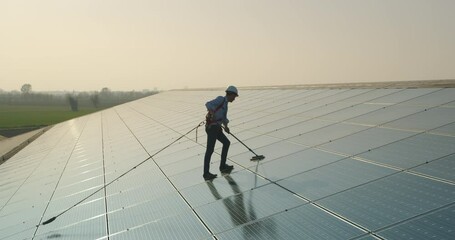 Wall Mural - cinematic shot of maintenance assistance technical worker in uniform is cleaning photovoltaic solar 