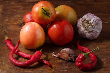 Close up shot of unripe tomatoes, garlic, red chilli hot peppers on wooden table. Healthy vegan food, seasonal fresh farm organic products