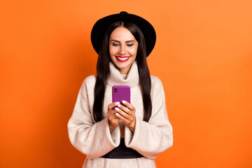 Poster - Photo of adorable shiny young woman wear beige sweater headwear typing modern device isolated orange color background