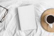 White book mockup with a cup of coffee and a glasses on the bed.