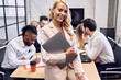 © Roman - Confident young woman in formal clothes, smiling with laptop in hads and looking on the camera sitting on the edge of the table in the office