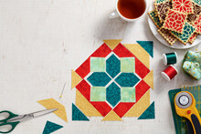 Pieces Of Fabric Laid Out In The Shape Of A Patchwork Block, A  Heap Of Cookies With A Pattern Imitating A Patchwork Block, A Cup Of Tea, Sewing And Quilting Accessories
