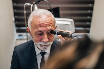 Wall Mural - Elegant senior bearded man receiving ophthalmology treatment. Doctor ophthalmologist checking his eyesight with modern equipment.