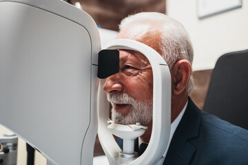 Elegant senior bearded man receiving ophthalmology treatment. Doctor ophthalmologist checking his eyesight with modern equipment.