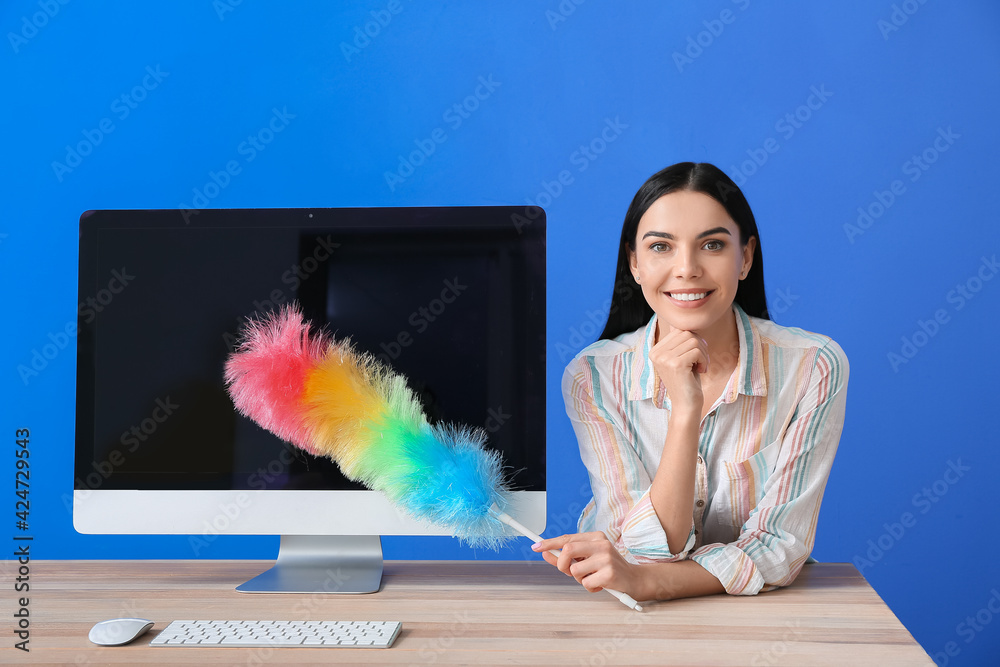 Young woman cleaning computer on color background