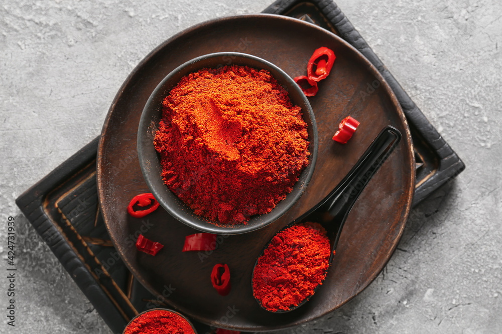 Bowl and spoon with red chili powder on grey background