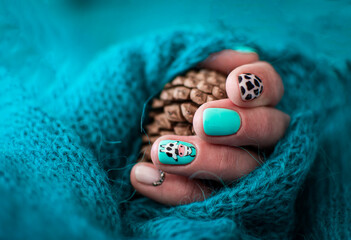 Colorful spring nail design with animal motives. Painted cow on a nail. Pine cone in a palm, isolated in crochet background. Selective focus on a nail, blurred background.