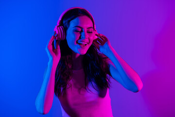 Canvas Print - Photo of young smiling excited beautiful gorgeous girl listening music in headphones isolated on blue neon color background