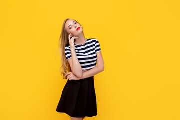 Wall Mural - Shy girl smiling looking to the camera. Caucasian charming girl with long hair wearing stripped t-shirt, standing against yellow studio background having fun