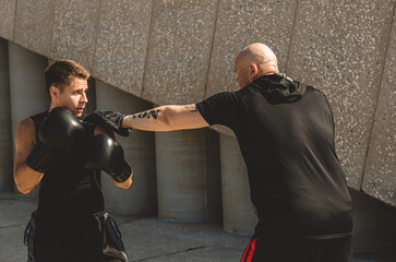 Sticker - Two men exercising and fighting in outside. Boxer in gloves is training with a coach