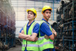© Stella - Portrait of two industrial engineer workers man wearing helmet with arms crossed, standing at manufacturing plant factory with many engine parts as blurred background