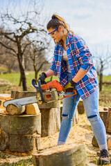 Wall Mural - Young Woman using chainsaw to cut a log for firewood.