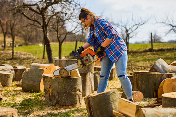 Wall Mural - Young Woman using chainsaw to cut a log for firewood.