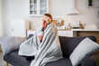 © DSMT - Young man sits on the sofa with a cup of tea wrapped in a blanket and is sick