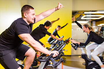 Pretty authentic female instructor with headset in fitness class exercise with group in cycling room