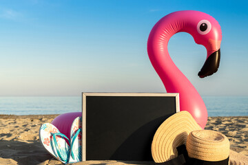 Wall Mural - Tropical background. Funny pink toy flamingo with blackboard, slippers and hat for text on summer ocean nature beach background in sunny tropical day. Funny bird toy for kids.