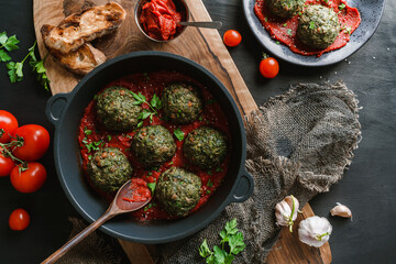 Wall Mural - Vegan spinach balls or cutlets with chickpeas in pan with tomato sauce and herb on dark wooden background. Healthy food, clean eating, vegetarian diet, top view