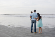 Family Of Three Standing On The Beach By The Ocean Looking Out Towards The Horizon, Coronado California