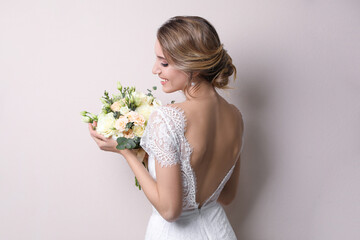 Poster - Young bride with elegant hairstyle holding wedding bouquet on beige background