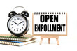 Open enrollment. text on white notepad paper on a stand next to our desk clock on a sideboard. on white background