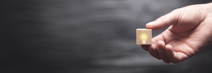 Wall Mural - Hand holding light bulb on wooden cube.