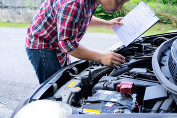 Automobile mechanic repairman checking a car engine with inspecting writing to the clipboard the checklist