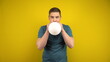 © Vital9c - A young man inflates a white balloon with his mouth on a yellow background. Man in a green polo.
