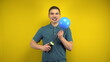 © Vital9c - A young man inflates a blue balloon with a pump on a yellow background. Man in a green polo.