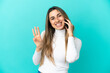 © luismolinero - Young caucasian woman using mobile phone isolated on blue background happy and counting three with fingers
