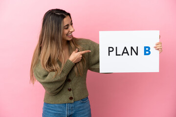 Wall Mural - Young caucasian woman isolated on pink background holding a placard with the message PLAN B