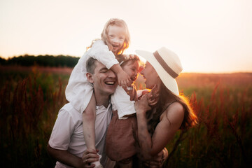 Stylish charming Caucasian young family with two children hugging in summer at sunset, girl kid blond with Down syndrome with parents and younger sister, brown chocolate tinting, family values