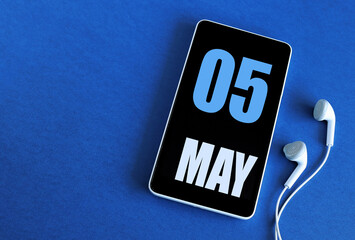 may 5. 5 st day of the month, calendar date. smartphone and white headphones on a blue background. p