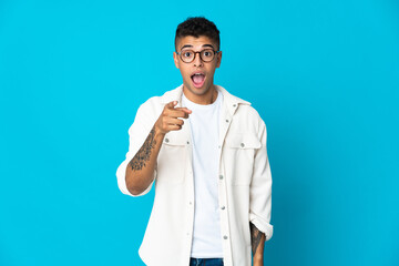 Young Brazilian man isolated on blue background surprised and pointing front