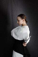 Beautiful young woman in a white Asian suit on a black background. The style of a modern geisha in the studio.