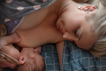 Young mother holding on hands  newborn two weeks baby at home in the room. Home portrait of  happy beautiful mother breastfeeding her newborn child in bedroom