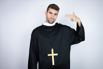 Wall Mural - Young hispanic man wearing priest uniform standing over white background Shooting and killing oneself pointing hand and fingers to head like gun, suicide gesture.