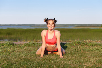 Young beautiful woman practicing yoga asana of a Simhasana lion pose on green grass near the lake at summer nature.